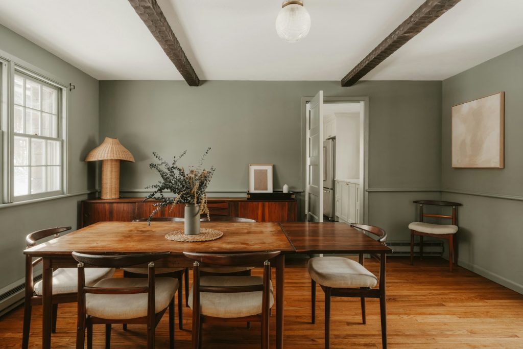 Eetkamer met groene wanden, houten tafel en een hanglamp in het midden