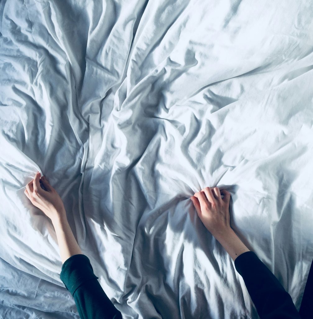 Handen strijken een wit hoeslaken glad over een matras