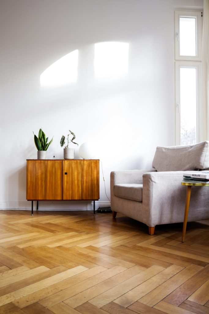 Laag houten dressoir met planten naast een lichte fauteuil