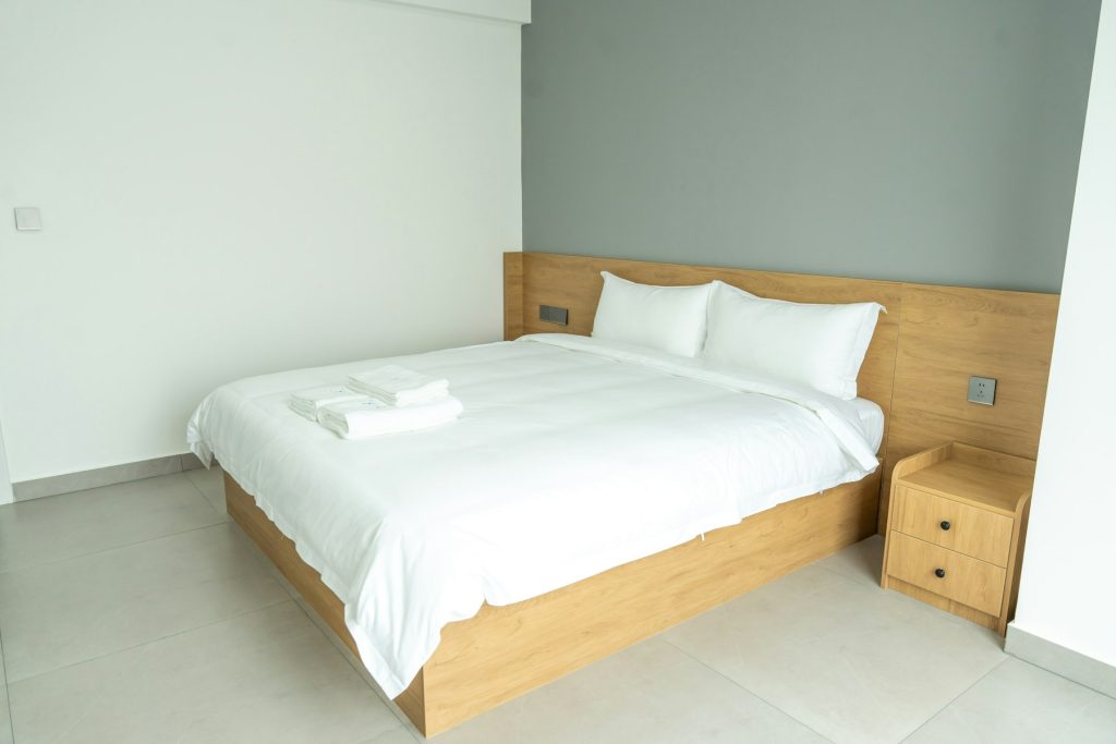 Opgemaakt bed met wit beddengoed en een houten frame in een lichte slaapkamer