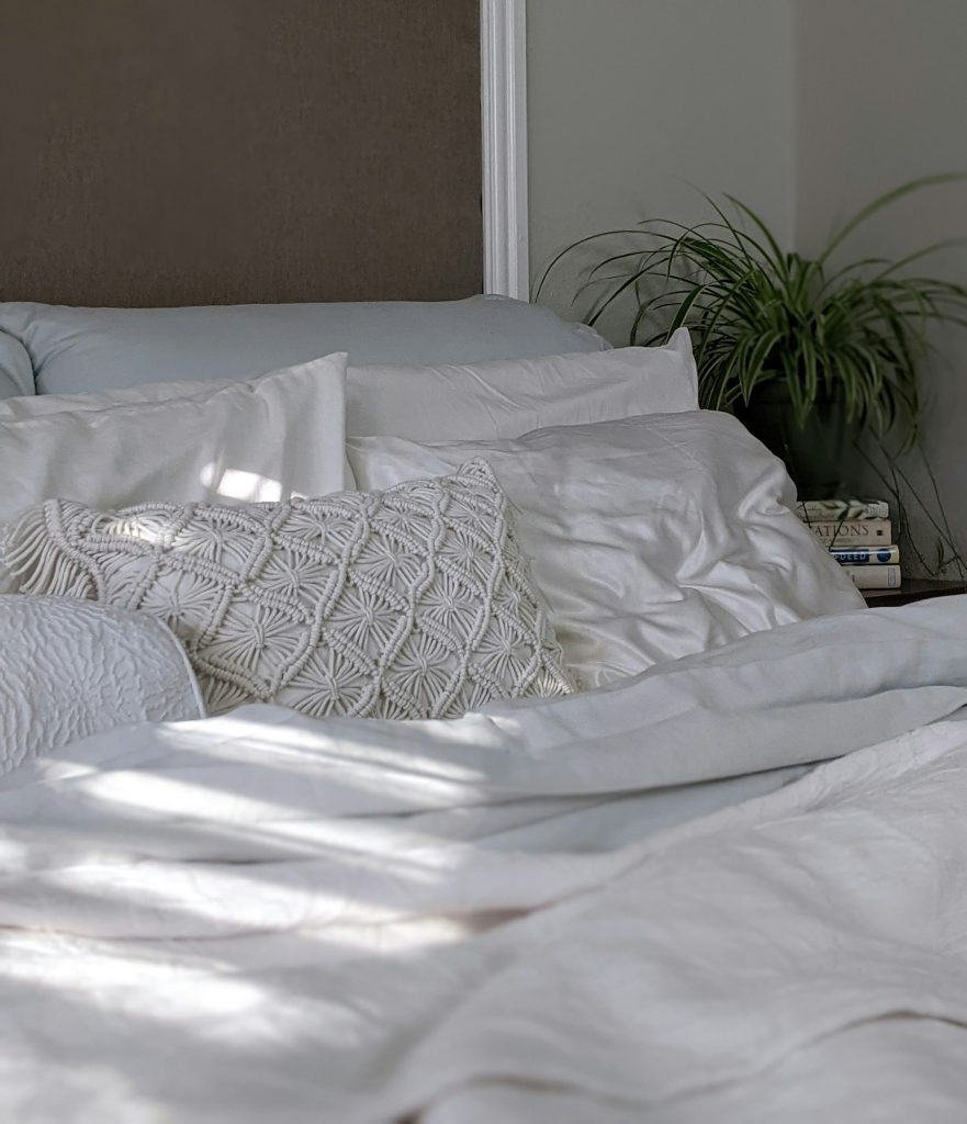 Opgemaakt bed met witte kussens, een gebreid kussen en een plant