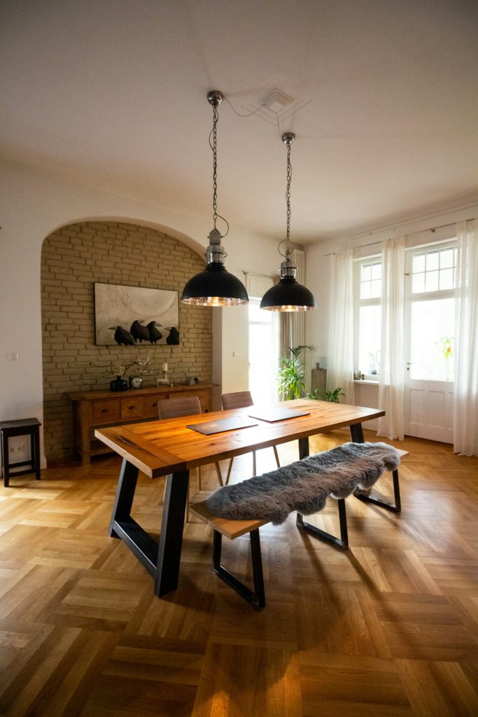 Twee zwarte industriële hanglampen boven een houten eettafel met bank