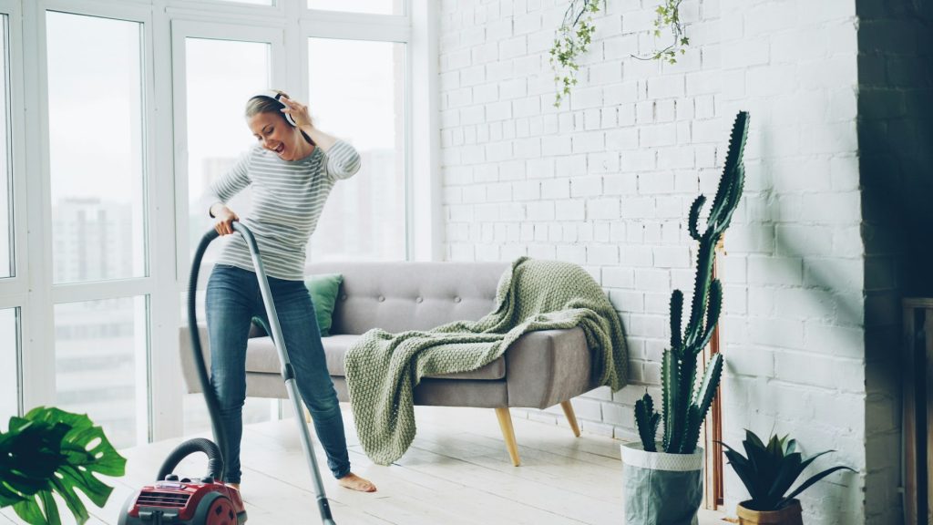 Vrouw stofzuigt een lichte woonkamer met een bank en een plaid