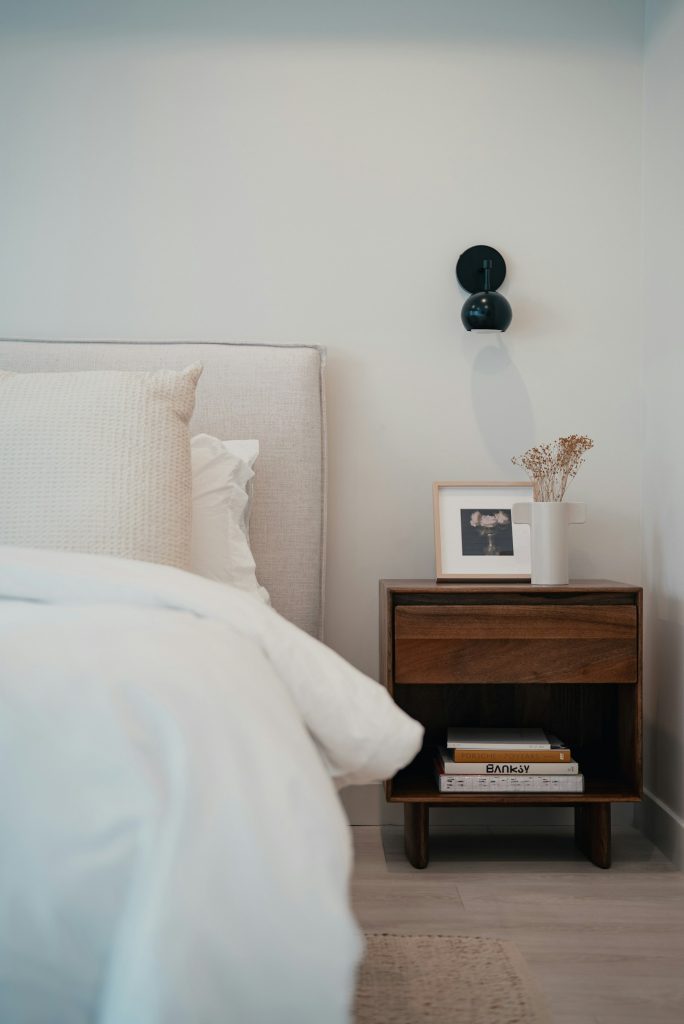 Wit gestoffeerd bed met een houten nachtkastje en een fotolijst