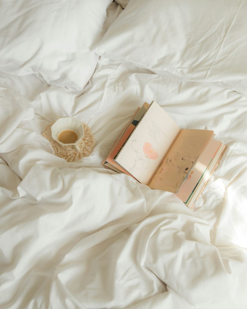 Wit opgemaakt bed met een opengeslagen boek en kaars