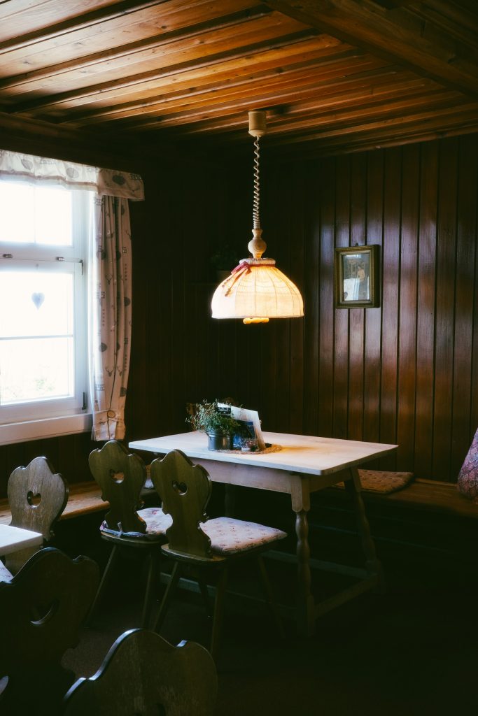 Witte lamp met warm licht boven een tafel tegen een houten wand