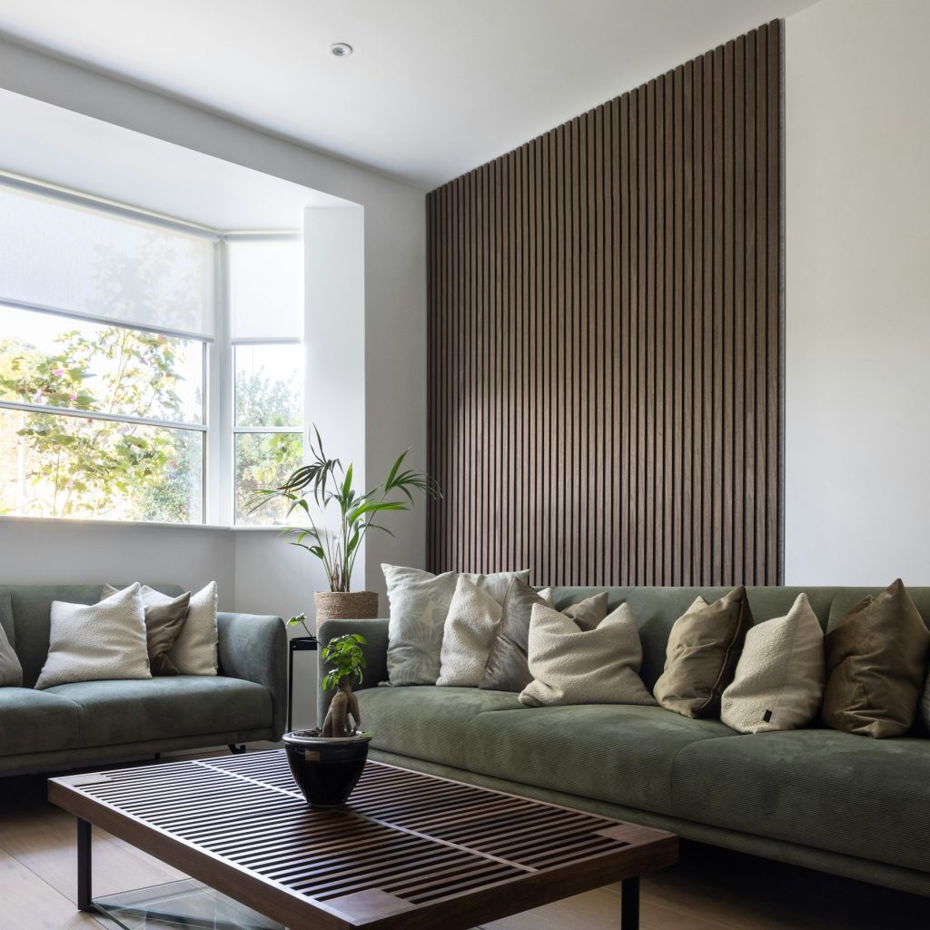 Woonkamer met een wand van donkere houten lamellen achter een groene bank
